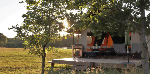 Tienda safari Classic Wood en Huttopia De Roos, Países Bajos, con terraza y sol atravesando árboles.