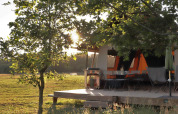 Tienda safari Classic Wood en Huttopia De Roos, Países Bajos, con terraza y sol atravesando árboles.