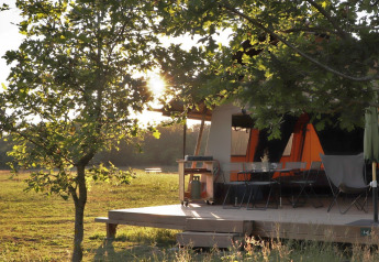 Tienda safari Classic Wood en Huttopia De Roos, Países Bajos, con terraza y sol atravesando árboles.
