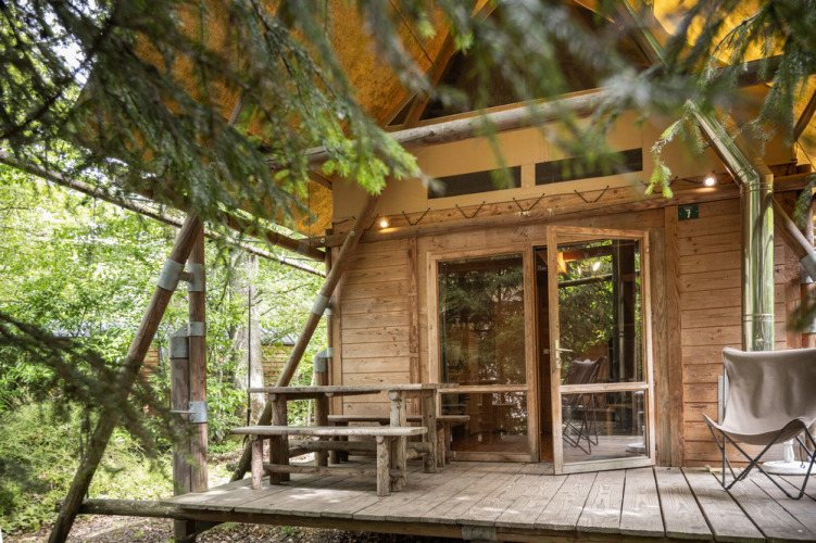 Tienda de safari Cahutte en Huttopia De Roos, Países Bajos, rodeada de árboles y terraza de madera rústica.