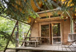 Tienda de safari Cahutte en Huttopia De Roos, Países Bajos, rodeada de árboles y terraza de madera rústica.
