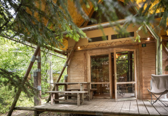 Tienda de safari Cahutte en Huttopia De Roos, Países Bajos, rodeada de árboles y terraza de madera rústica.