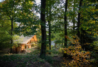 Tienda tipo safari Cahutte rodeada de árboles verdes en Huttopia De Roos, Países Bajos, durante el día.