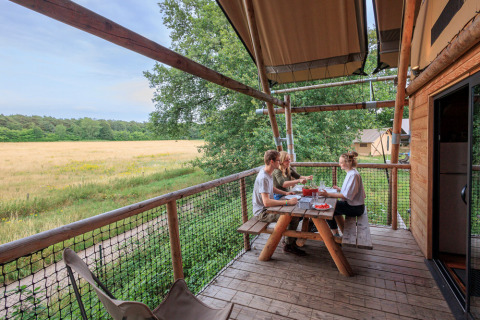 Tres personas disfrutan de una comida en la terraza de una tienda safari en Cahutte, Huttopia De Roos, Países Bajos.