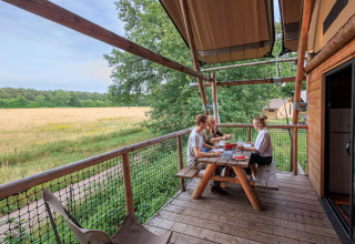 Tres personas disfrutan de una comida en la terraza de una tienda safari en Cahutte, Huttopia De Roos, Países Bajos.