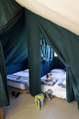 Interior de una tienda safari Cahutte en Huttopia De Roos, Países Bajos, con camas y juguetes.