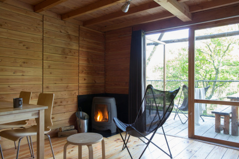 Vista interior de una acogedora cabaña safari con estufa de leña y grandes ventanales hacia la naturaleza.