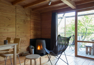 Vista interior de una acogedora cabaña safari con estufa de leña y grandes ventanales hacia la naturaleza.
