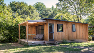 Blockhaus im Chalet Toronto mit überdachter Terrasse, Gartenmöbeln und Bäumen im Hintergrund.