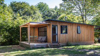 Cabaña de madera en Chalet Toronto con terraza cubierta, sillas y rodeada de árboles verdes.