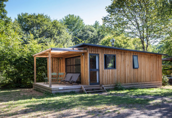 Cabaña de madera en Chalet Toronto con terraza cubierta, sillas y rodeada de árboles verdes.