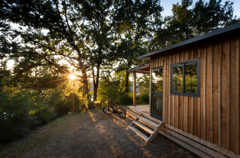 Zonsondergang bij Chalet Toronto, Huttopia De Roos, Nederland, met houten lodge, fiets en bosrijke omgeving.
