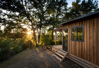 Zonsondergang bij Chalet Toronto, Huttopia De Roos, Nederland, met houten lodge, fiets en bosrijke omgeving.