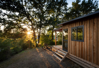 Atardecer en Chalet Toronto, Huttopia De Roos, Países Bajos, con cabaña de madera, bicicleta y bosque.