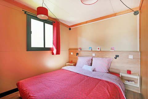 Slaapkamer in Chalet Toronto bij Huttopia De Roos, Nederland, met tweepersoonsbed en rode accenten.