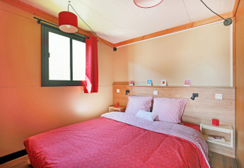 Slaapkamer in Chalet Toronto bij Huttopia De Roos, Nederland, met tweepersoonsbed en rode accenten.