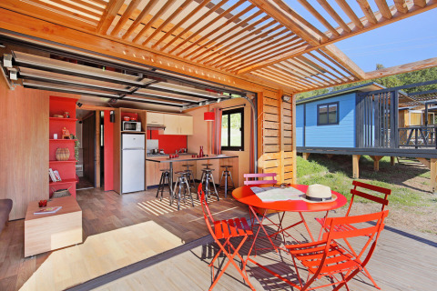 Licht en modern chalet met open keuken en rood tuinmeubilair bij Huttopia De Roos in Nederland.