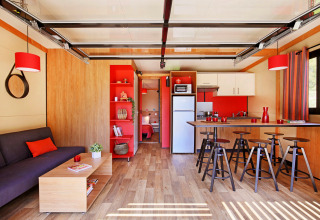 Modernes Wohnzimmer und Küche im Chalet Toronto bei Huttopia De Roos, Niederlande, mit roten Akzenten.