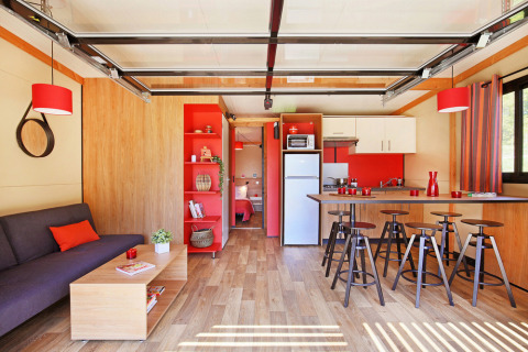 Moderne woonkamer en keuken in Chalet Toronto bij Huttopia De Roos, Nederland, met rode accenten en hout.