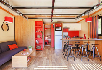 Sala y cocina modernas en el Chalet Toronto de Huttopia De Roos, Países Bajos, con detalles rojos y madera clara.