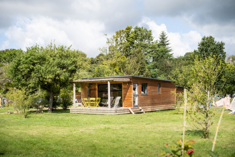 Houten chalet bij Chalet Toronto, Huttopia De Roos in Nederland, omringd door groene bomen en weide.