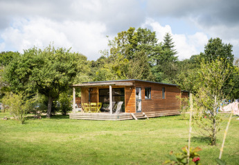 Houten chalet bij Chalet Toronto, Huttopia De Roos in Nederland, omringd door groene bomen en weide.