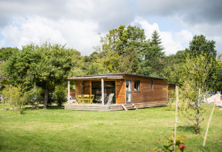Cabaña de madera en Chalet Toronto, Huttopia De Roos, Países Bajos, rodeada de árboles verdes y césped.