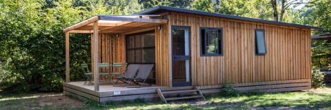 Houten chalet met overdekt terras en zitjes, omgeven door groen op Huttopia De Roos in Nederland.
