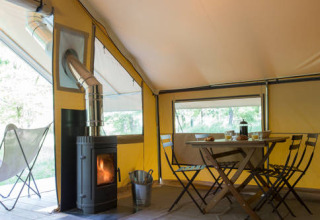 Binnenkant van de Trappeur tent met eettafel, stoelen en houtkachel bij Huttopia Lac de l'Uby - Gers, Frankrijk.