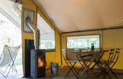 Interior of the Trappeur tent with dining table, chairs, and wood stove at Huttopia Lac de l'Uby - Gers, France.