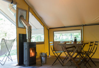 Interior of the Trappeur tent with dining table, chairs, and wood stove at Huttopia Lac de l'Uby - Gers, France.