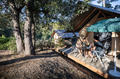Family relaxing outside a Trappeur safari tent at Huttopia Lac de l'Uby - Gers, France, surrounded by nature.