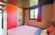 Dormitorio acogedor con detalles rojos en Gypsy caravan en Huttopia Parque de Doñana, España, con ventana.