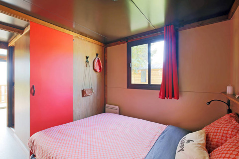 Schlafzimmer im Gypsy caravan im Huttopia Parque de Doñana, Spanien, mit roter Deko und großem Fenster.