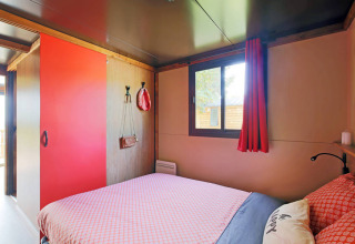 Schlafzimmer im Gypsy caravan im Huttopia Parque de Doñana, Spanien, mit roter Deko und großem Fenster.