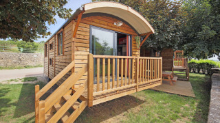 Cabane en bois nommée Gypsy caravan avec terrasse et escalier, entourée d'arbres et d’herbe verdoyante.