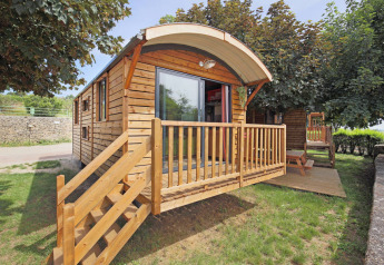 Blockhütte namens Gypsy caravan mit Holzveranda und Treppe, umgeben von Bäumen und grünem Rasen.