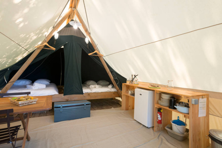 Interior de una tienda safari Canadienne con camas, cocina y mesa en Huttopia Parque de Doñana, España.