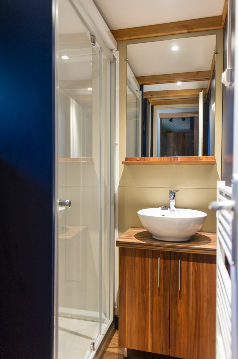 Moderne badeværelse i Chalet Evasion glamping med træskab, rund vask og glasbruseniche.
