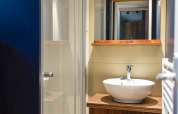 Moderne badeværelse i Chalet Evasion glamping med træskab, rund vask og glasbruseniche.