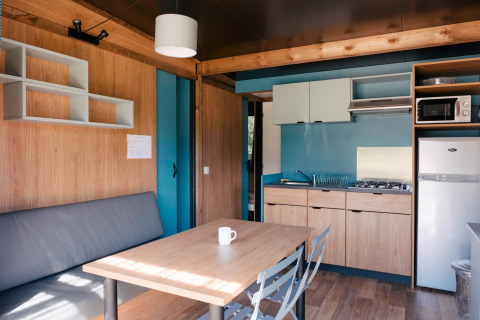 Moderne glamping Chalet Evasion indretning med køkken, spisebord, sofa og køleskab, lyse træpaneler.