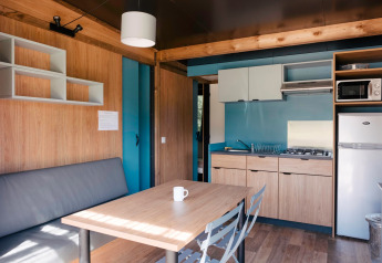 Interieur van glamping Chalet Evasion met moderne keuken, eettafel, bank, koelkast en houten afwerking.
