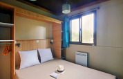 Glamping-Zimmer im Chalet Evasion mit Doppelbett, großem Fenster, hellen Kissen und offener Garderobe.