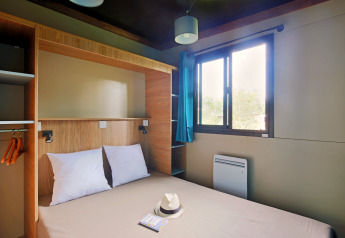Chambre glamping au Chalet Evasion avec lit double, fenêtre lumineuse, rideaux bleus et espace de rangement.