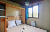 Habitación glamping en Chalet Evasion con cama doble, ventana luminosa, cortinas azules y armario abierto.