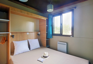 Moderne glampingværelse i Chalet Evasion med dobbeltseng, vindue, blå gardiner og opbevaringsplads.