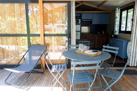 Terraza con mesa, sillas y tumbona frente a cocina en Chalet Evasion, Huttopia Parque de Doñana, España.