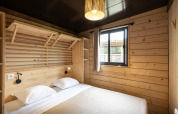 Moderne glamping-soveværelse i Chalet Portland med træpaneler, dobbeltseng og et vindue med lyse gardiner.