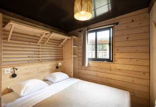 Modern glamping bedroom at Chalet Portland with wooden walls, double bed, window, and light curtain.