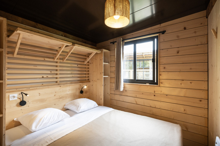 Moderne glamping slaapkamer in Chalet Portland met houten muren, dubbel bed en raam met lichtgordijn.